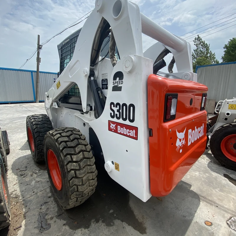 Боковой вид мини-погрузчика Bobcat S300 с опущенным универсальным ковшом.