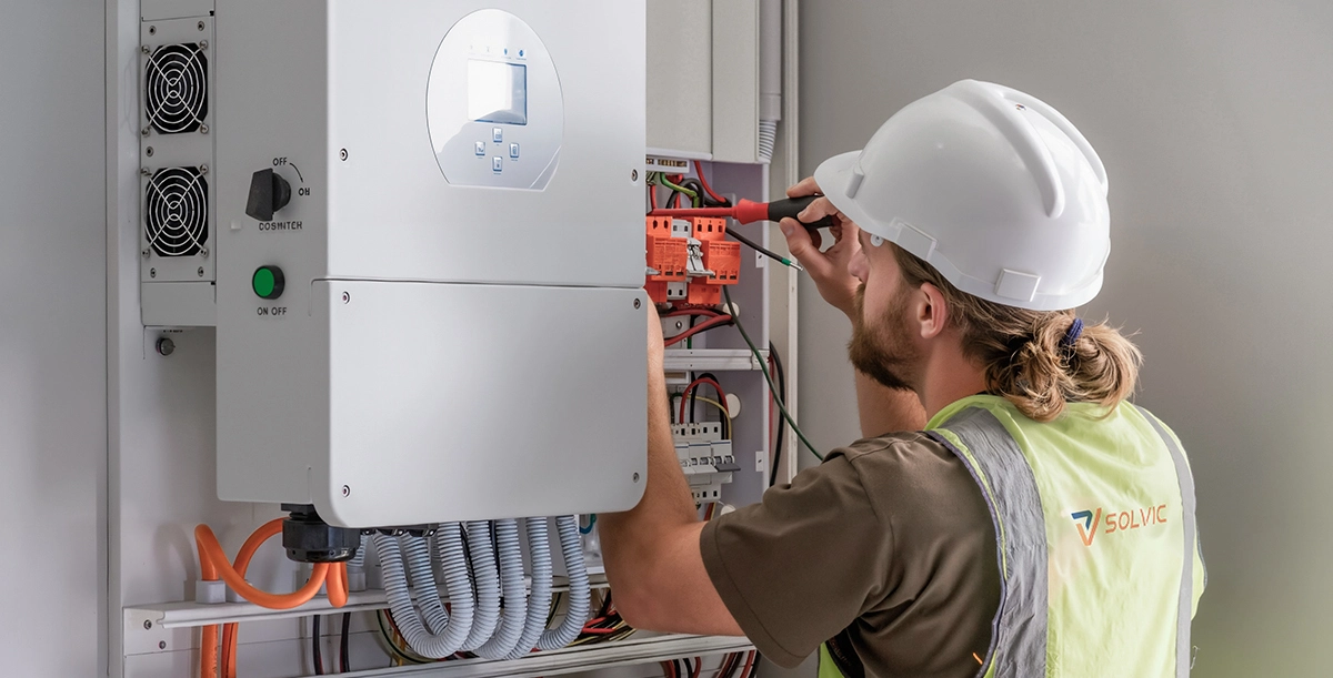Technician installing solar hybrid inverter wiring – Solvic Power professional installer connecting PV input, battery and grid cables to wall-mounted inverter – residential energy storage installation